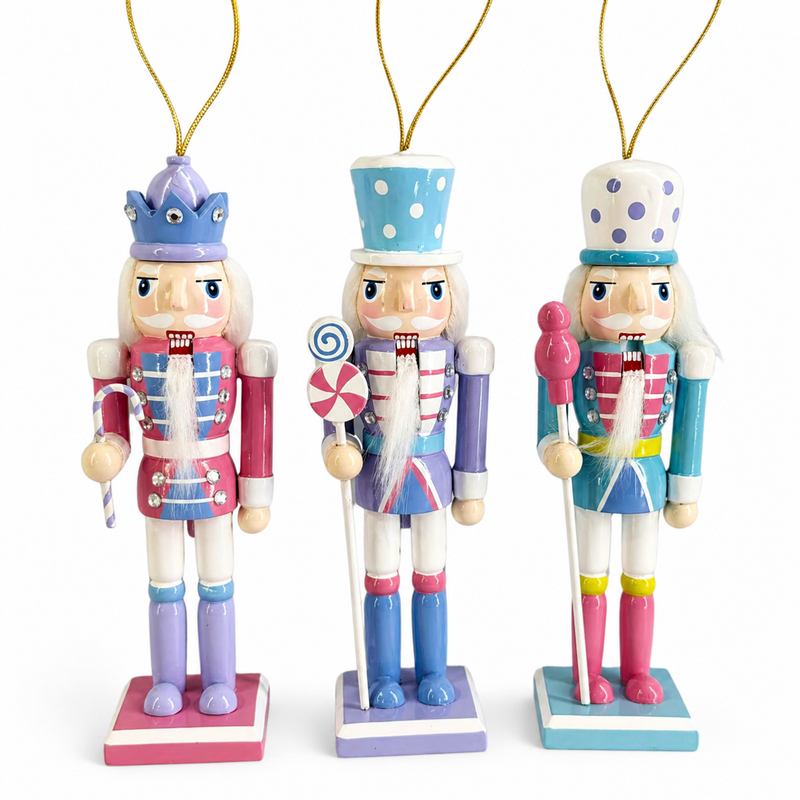 Set of three pastel candy nutcracker ornaments in pink, purple, and teal, each holding a different candy accessory